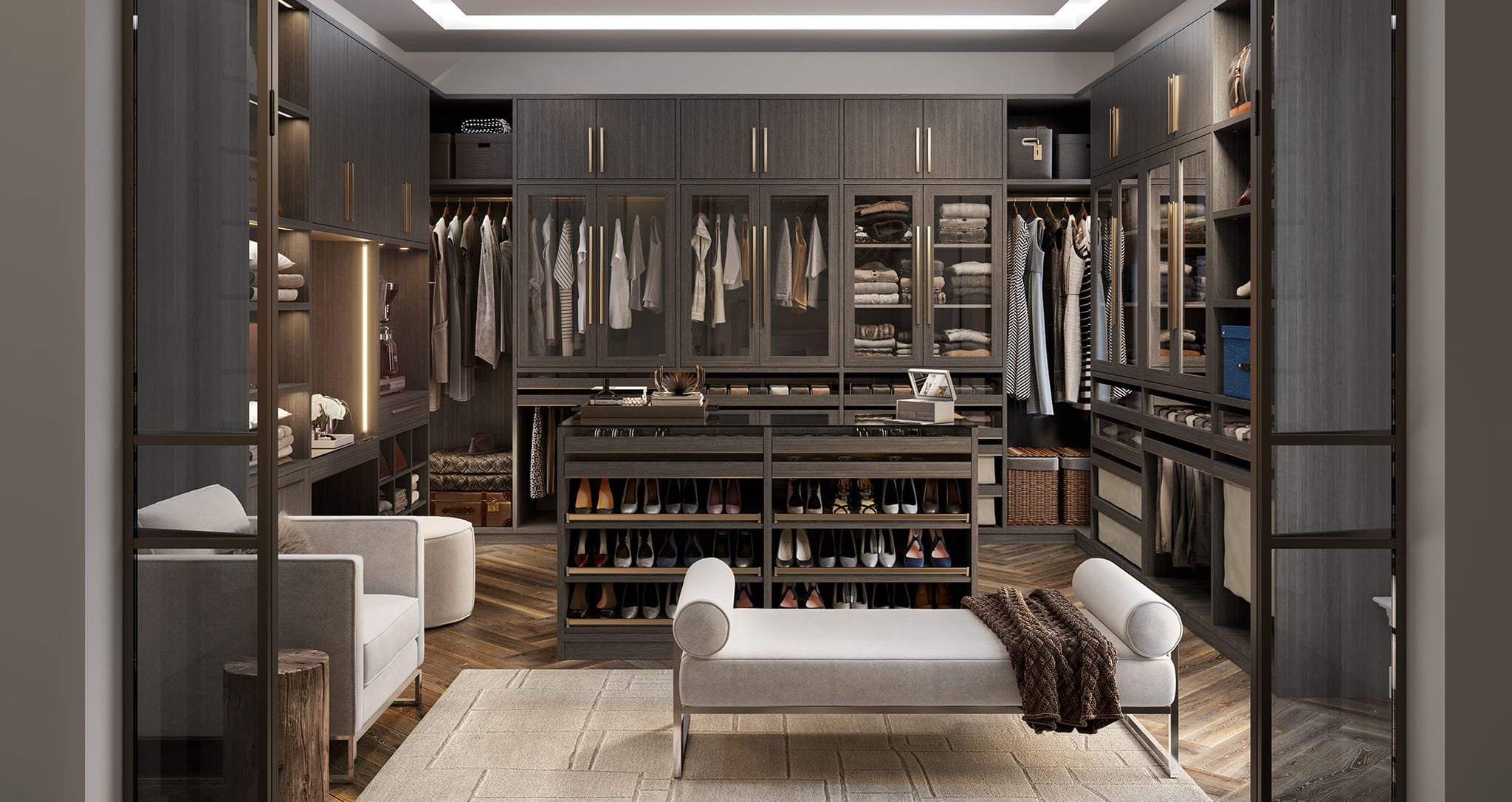 Closet design in u-shape in modern dark wood grain finish with custom shoe storage, glass door cabinets and center seating by California Closets
